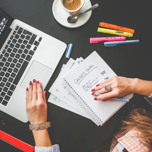 women one hand on laptop and other hand on notebook